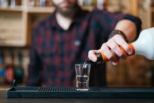 Knappe bebaarde barman maakt apenhersencocktail in nachtclub. Selectieve focus op glas.