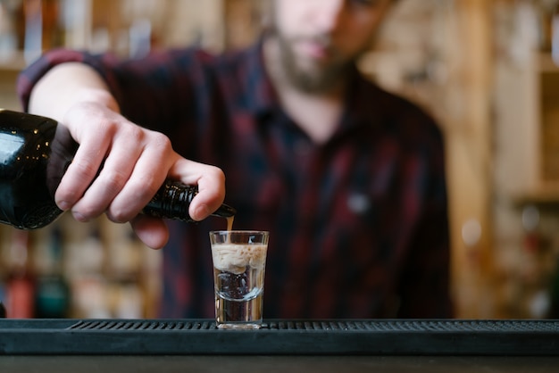 Knappe bebaarde barman maakt apenhersencocktail in nachtclub. Selectieve focus op glas.