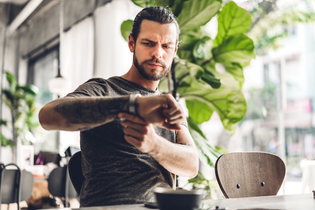 Knappe bebaarde hipster man kijken horloge met koffie zittend aan tafel in café