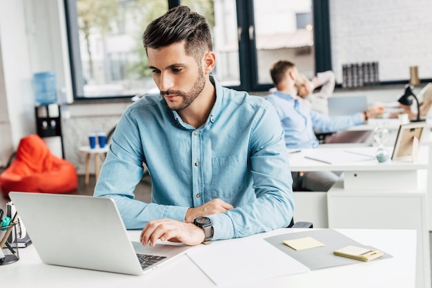 Knappe bebaarde jonge zakenman die laptop gebruikt op de werkplek