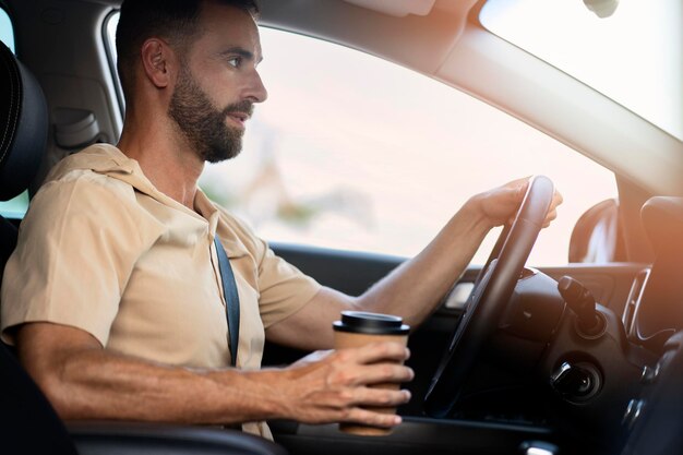 Knappe bebaarde Latijns-man rijdende auto met kopje koffie. Vervoer, roadtrip