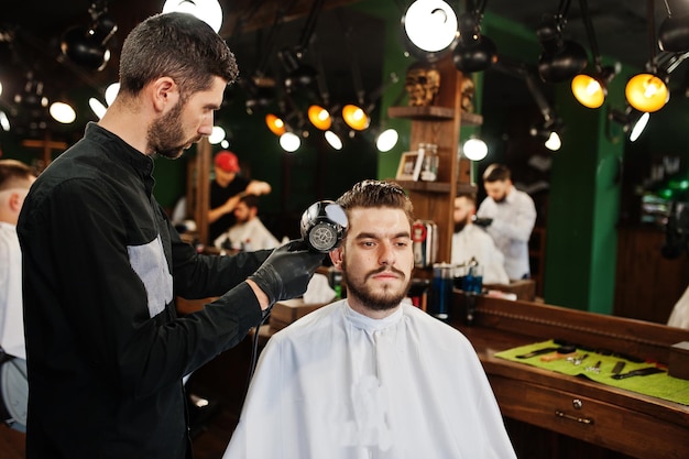 Knappe bebaarde man bij de kapperszaak kapper op het werk met föhn