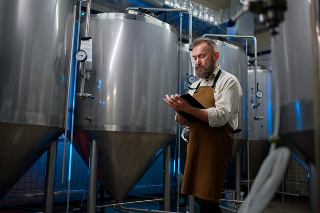 Foto knappe bebaarde man brouwer in moderne bierfabriek rond stalen tanks