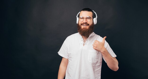 Knappe bebaarde man houdt een duim omhoog en draagt een headset die naar een podcast of wat muziek luistert.