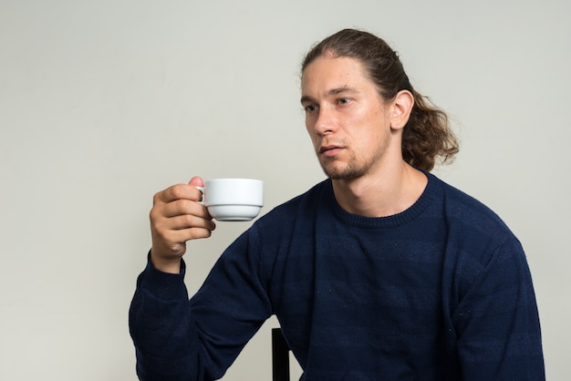 knappe bebaarde man met lang haar tegen witte muur