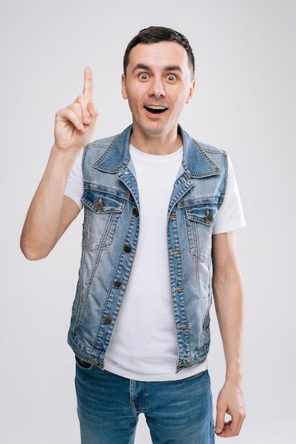 Knappe blanke jonge man in denim kleding kijken naar de camera en omhoog wijzend op een witte achtergrond.