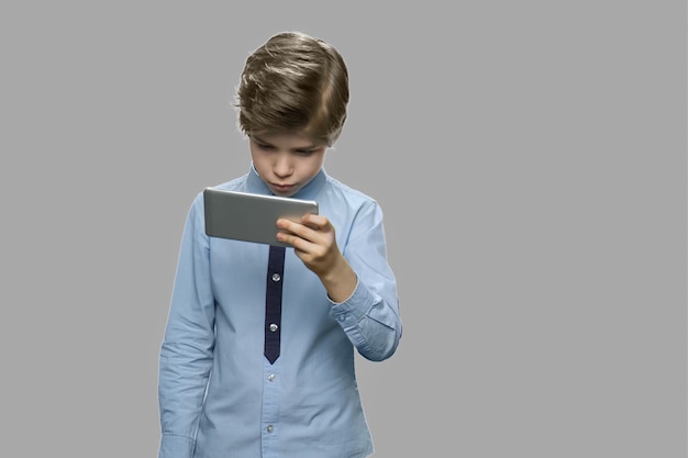 Knappe blanke jongen met behulp van smartphone. Weinig jongen die celtelefoon op grijze achtergrond bekijkt. Vrije tijd, kinderen, technologie, internetverslaving en mensenconcept.