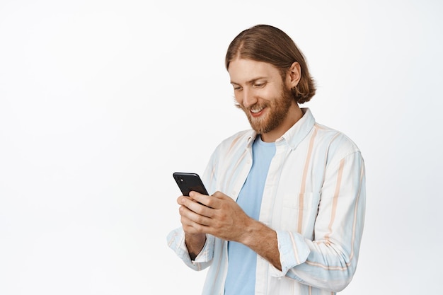 Knappe blanke man met behulp van mobiele telefoon, kijken naar scherm, witte achtergrond.