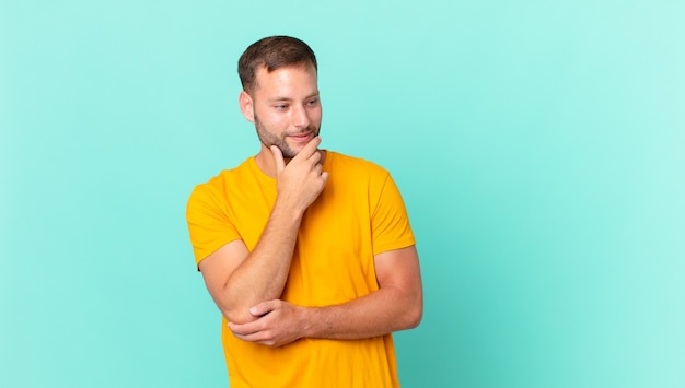 Knappe blonde man die lacht met een gelukkige, zelfverzekerde uitdrukking met de hand op de kin