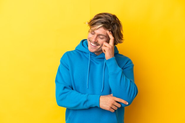 Knappe blonde man geïsoleerd op gele muur lachen