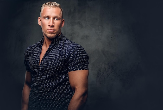 Knappe blonde man in een donkerblauw shirt poseren over grijze achtergrond in een studio.