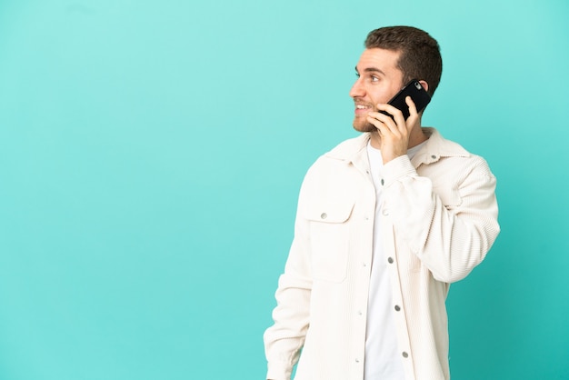 Knappe blonde man over geïsoleerde blauwe achtergrond die een gesprek voert met de mobiele telefoon met iemand