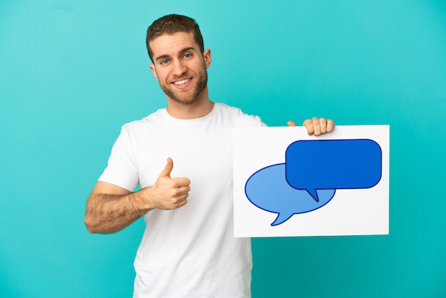 Knappe blonde man over geïsoleerde blauwe achtergrond met een plakkaat met tekstballon pictogram met duim omhoog