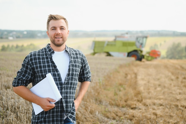 Knappe boer met tablet die voor de maaidorser staat tijdens de oogst in het veld