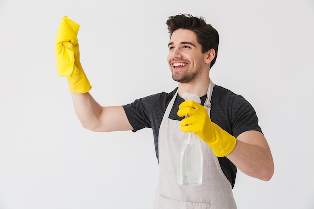 Knappe brunette huisman met schort geïsoleerd over wit, schoonmaken met een spons