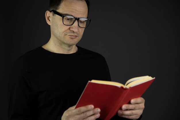 Knappe casual geklede jaren '40 man met donker haar in glazen leest nauwgezet rood boek