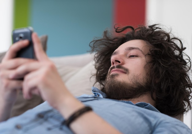 Knappe casual jonge man met behulp van een mobiele telefoon in luxe huis