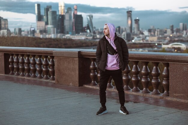 Knappe casual man in zwarte jas en roze hoody staande op een wolkenkrabber.