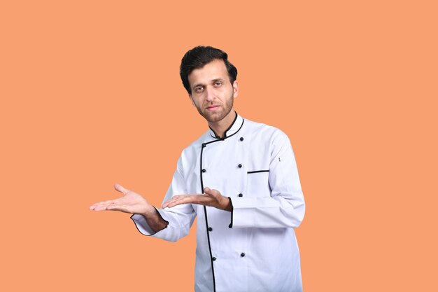 knappe chef-kok die iets over oranje achtergrond Indiaas Pakistaans model voorstelt