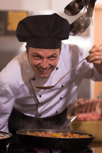 Knappe chef-kok die voedsel met lepel proeft bij de restaurantkeuken
