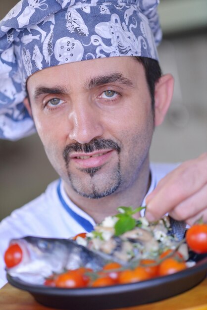 Knappe chef-kok gekleed in wit uniform decoreren pastasalade en zeevruchten vis in moderne keuken