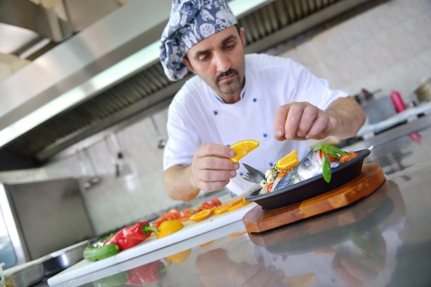 Knappe chef-kok gekleed in wit uniform decoreren pastasalade en zeevruchten vis in moderne keuken