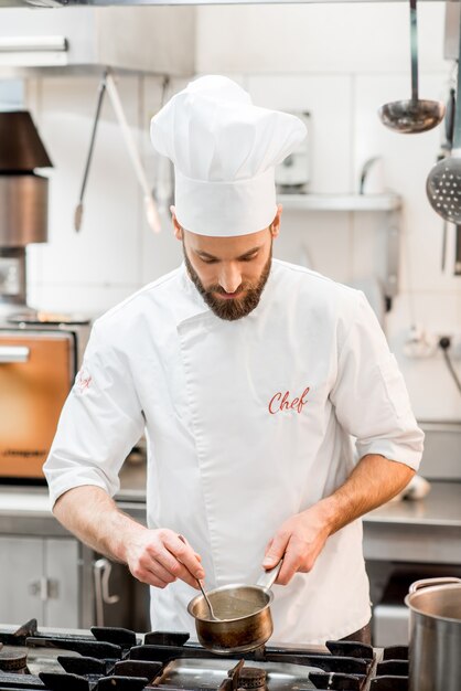 Knappe chef-kok in uniform koken van voedsel op het gasfornuis in de keuken van het restaurant