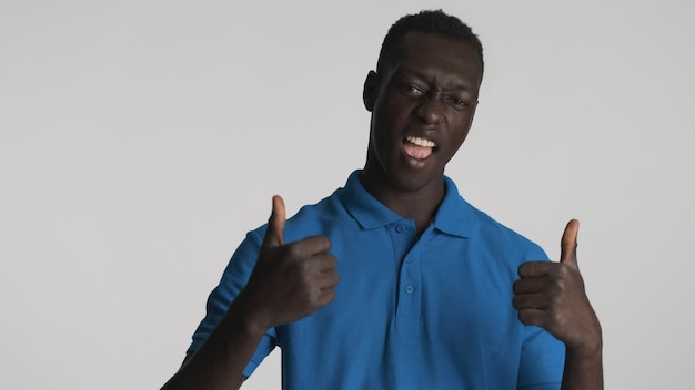 Knappe coole Afro-Amerikaanse man die duimen omhoog houdt en zich verheugt op camera op witte achtergrond