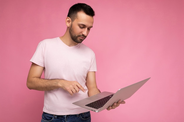 Knappe donkerbruine man die laptopcomputer houdt en op het toetsenbord typt die netbookmonitor in t-shirt bekijken