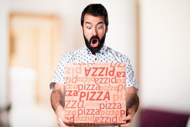 Knappe donkerbruine mens die met baard een pizza houdt