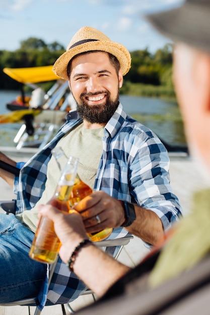 Knappe donkerharige man die flessen bier rammelt met een vriend tijdens het vissen