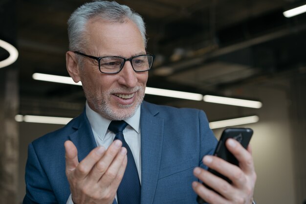 Knappe emotionele man met behulp van mobiele telefoon voor videoconferentie, werken in moderne kantoren