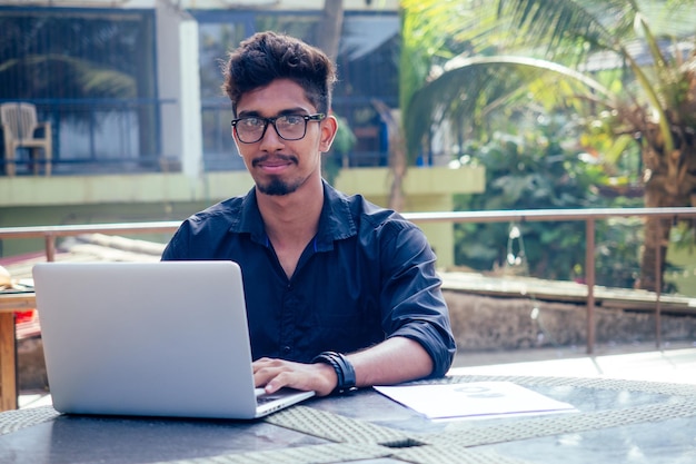 Knappe en jonge succesvolle Indiase man freelancen surfen op afstand werken met een laptop op het strand bij de ocean.india zakenman freelance programmering online copywriter paradijs landschap droombaan