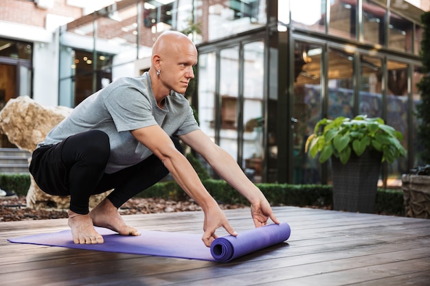 knappe geconcentreerde jonge yoga man met fitness tapijt buitenshuis.