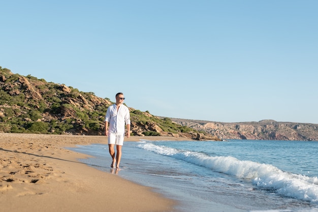 Knappe gelukkige man in wit overhemd wandelen op het strand