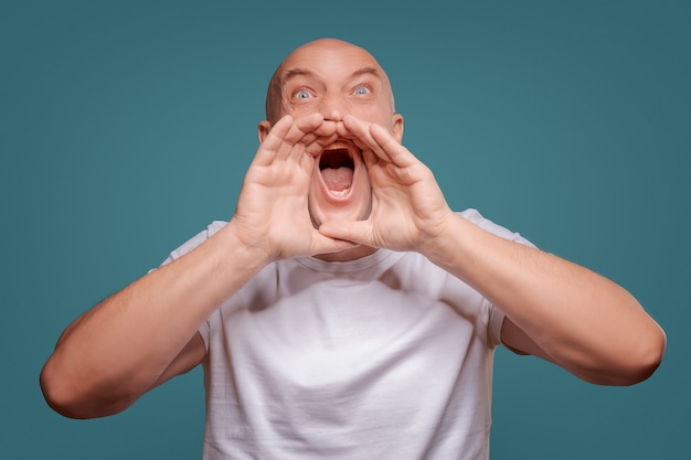 Knappe gelukkige mens die witte T-shirt, kerel draagt die luid spreekt, geïsoleerd op blauwe achtergrond