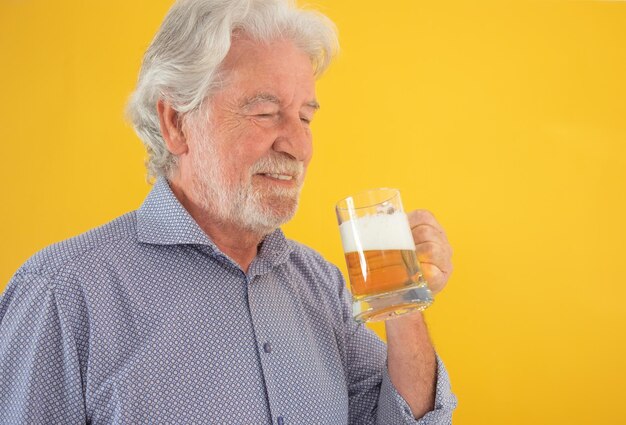 Knappe gelukkige senior man met een glas vers blond bier blanke bebaarde oudere man op gele achtergrond