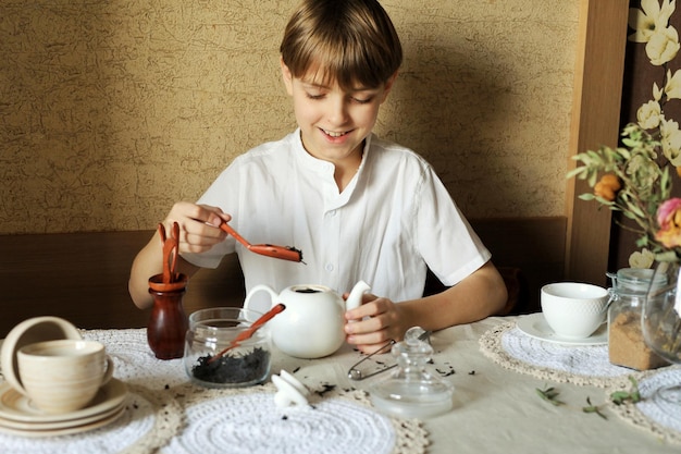 Knappe gelukkige tienerjongen die thuis aan tafel zit en zwarte thee maakt om te drinken