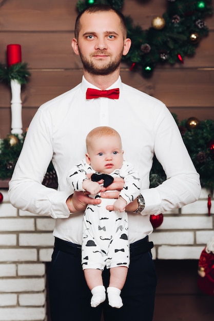 Knappe gelukkige vader in wit overhemd en stropdas die zoontje houden door handen