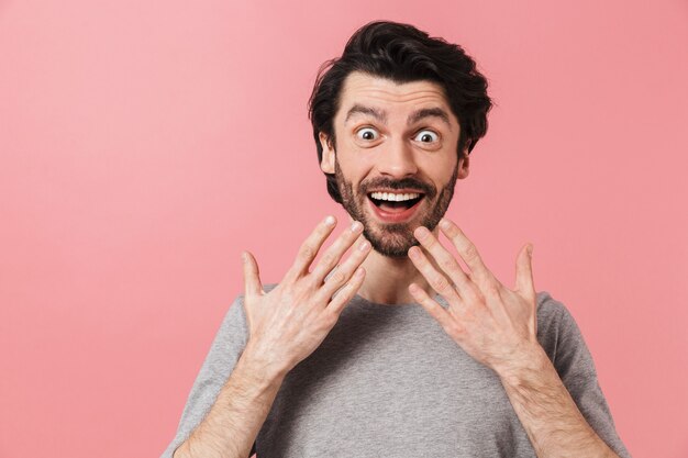 Knappe geschokt jonge bebaarde brunette man met trui permanent over roze, vieren