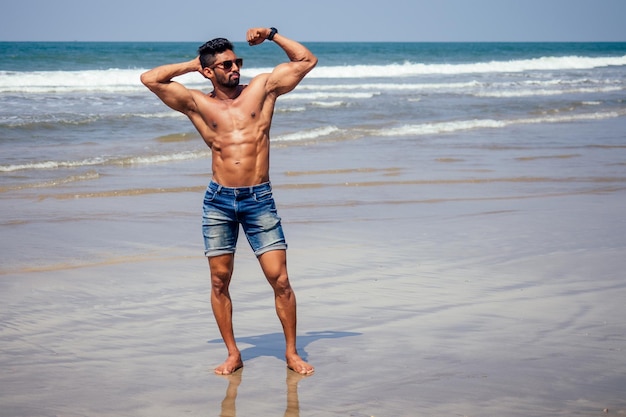 Knappe gespierde donkerharige surfer atletisch gespierde en gezonde zwarte man op het strand tijdens de zomerochtend opwarmen oceaan india zee Goa vakantie