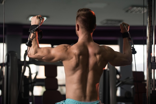 Knappe gespierde fitness bodybuilder doet zware oefening voor schouders op machine met kabel in de sportschool