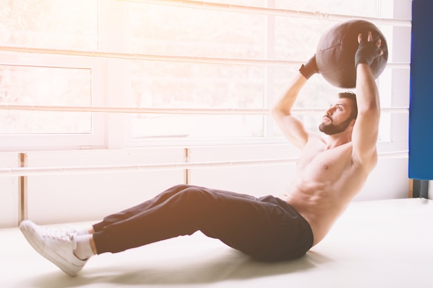 Knappe gespierde man doen sit-ups op een houten vloer.