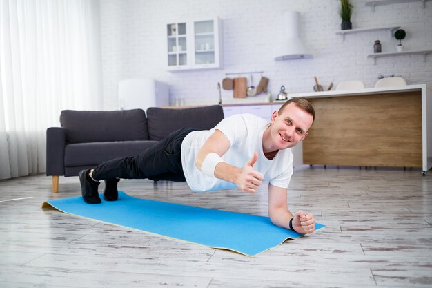 Knappe gespierde man in een t-shirt doet functionele oefeningen op de vloer thuis. Thuis fitnessen. Gezonde levensstijl.