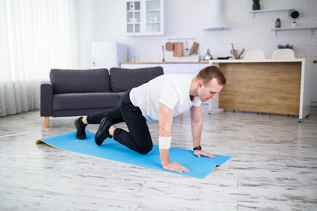 Knappe gespierde man in een t-shirt doet functionele oefeningen op de vloer thuis. Thuis fitnessen. Gezonde levensstijl.