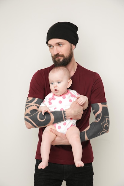 Knappe getatoeëerde jonge man met schattige kleine baby op lichte achtergrond
