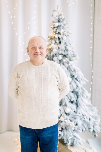 Knappe glimlachende blanke man van middelbare leeftijd in de buurt van de kerstboom