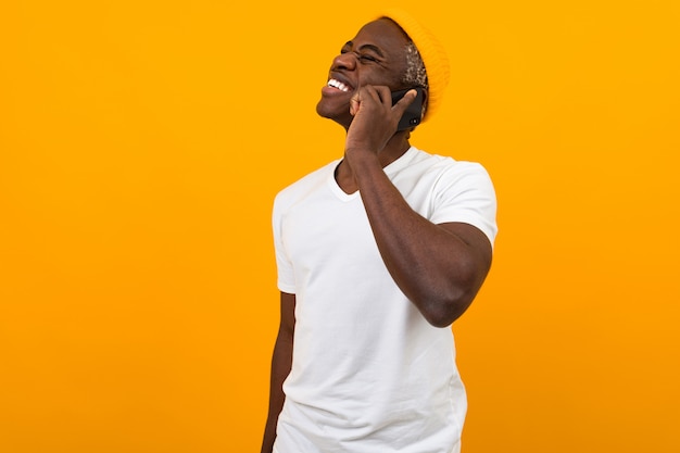 Knappe glimlachende donkere man in een wit t-shirt praten aan de telefoon op een oranje studio met