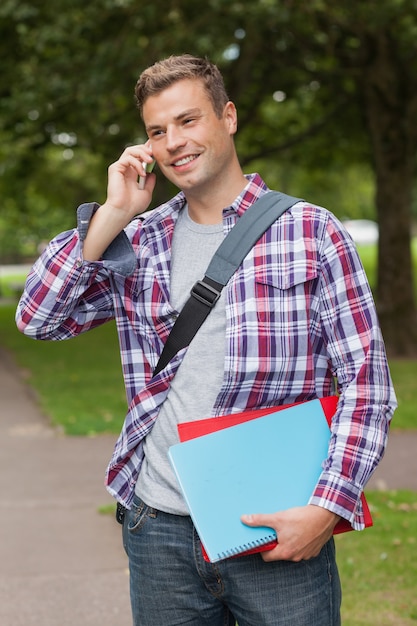 Knappe glimlachende student die en telefoneert bevindt zich