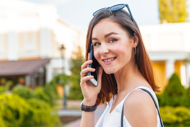 Knappe glimlachende vrouw die met mobiele telefoon op de straat loopt